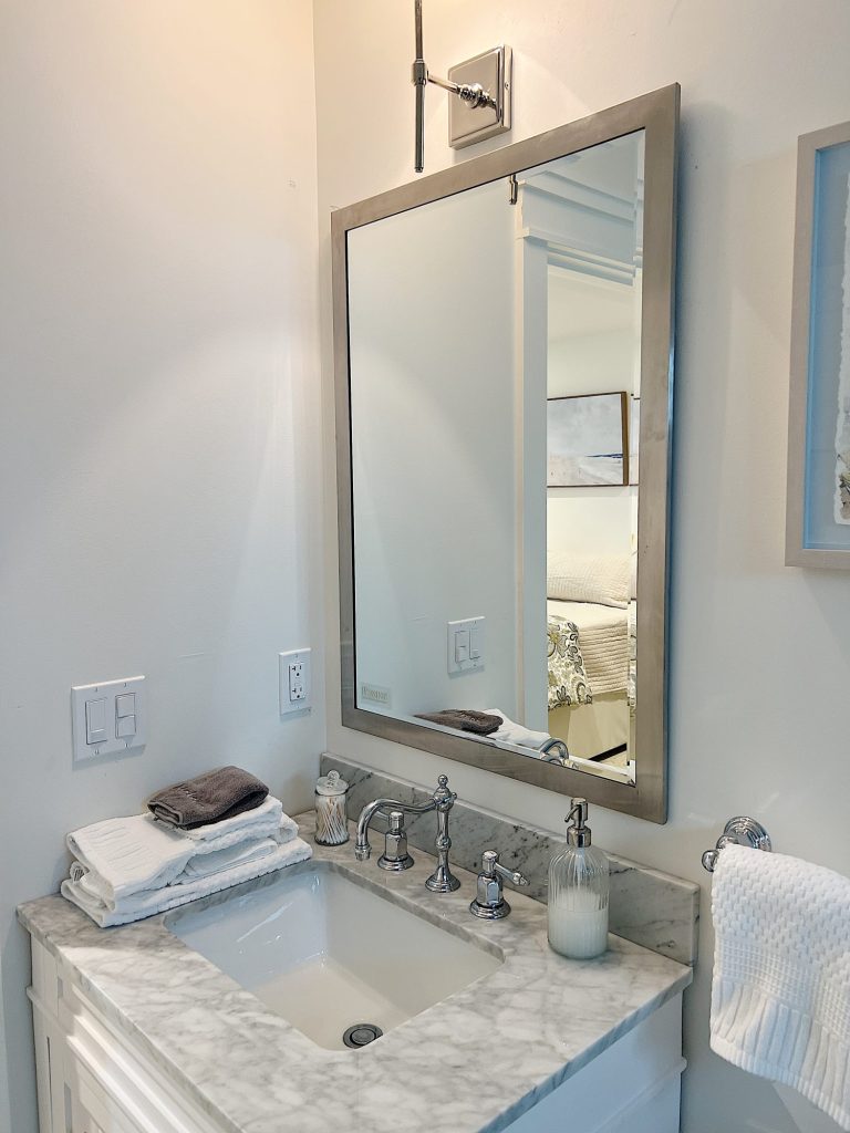 A bathroom mirror, sink with marble countertop and chrome fixtures.