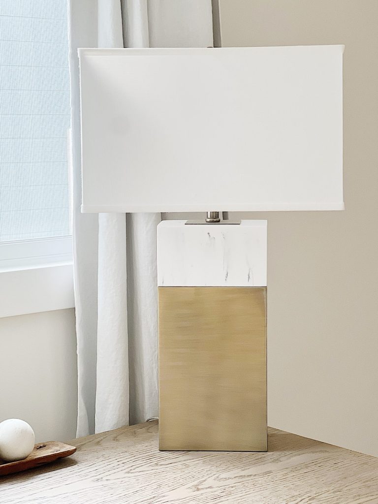 A marble and gold table lamp sitting on a wood desk.