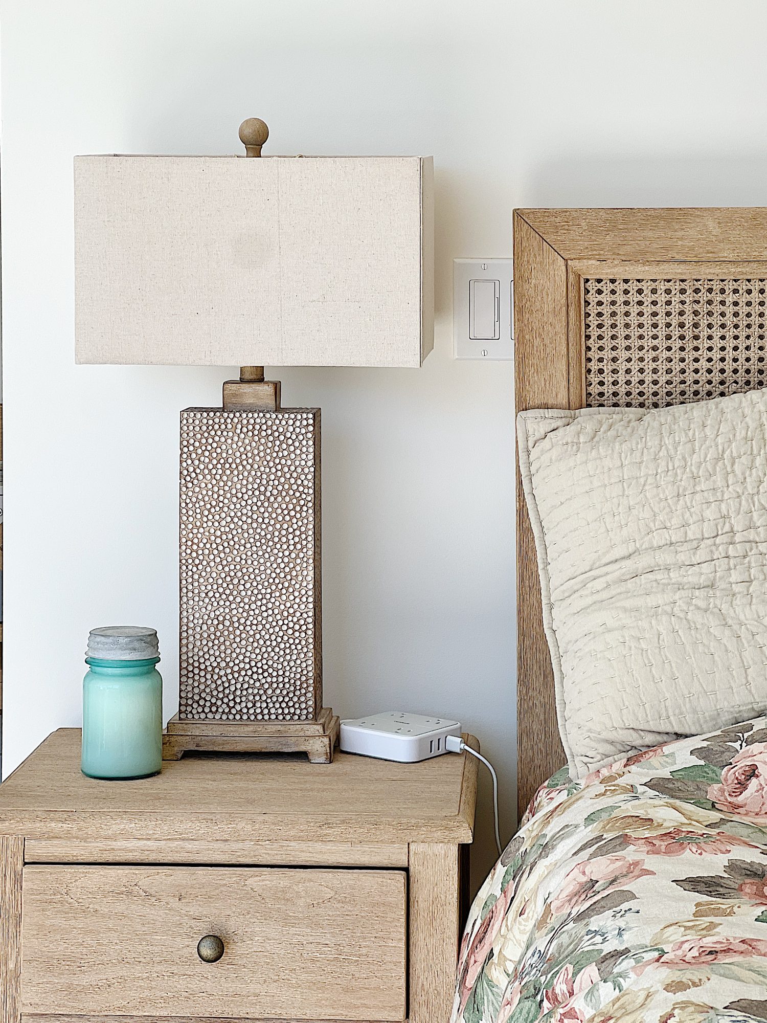 A bedroom with a polka dot lamp, a bed side table and a bed with floral bedding.