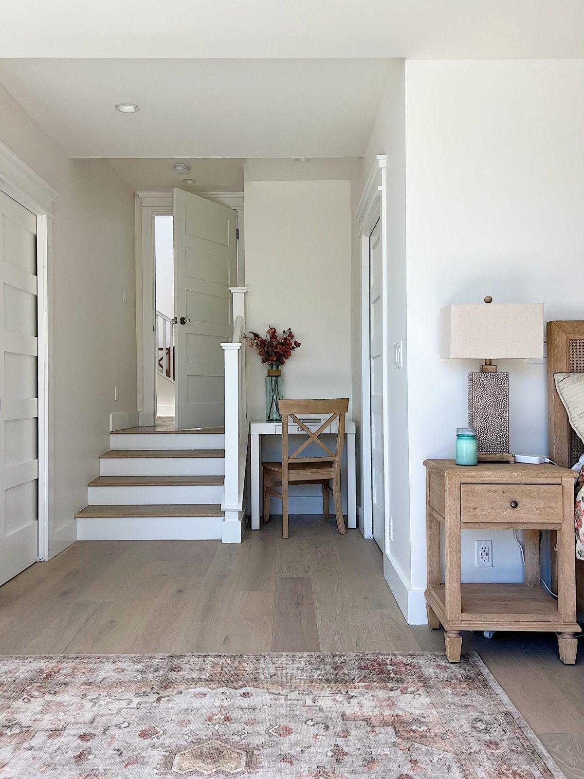 A bedroom with stairs, a small desk and a bedside table with a lamp.