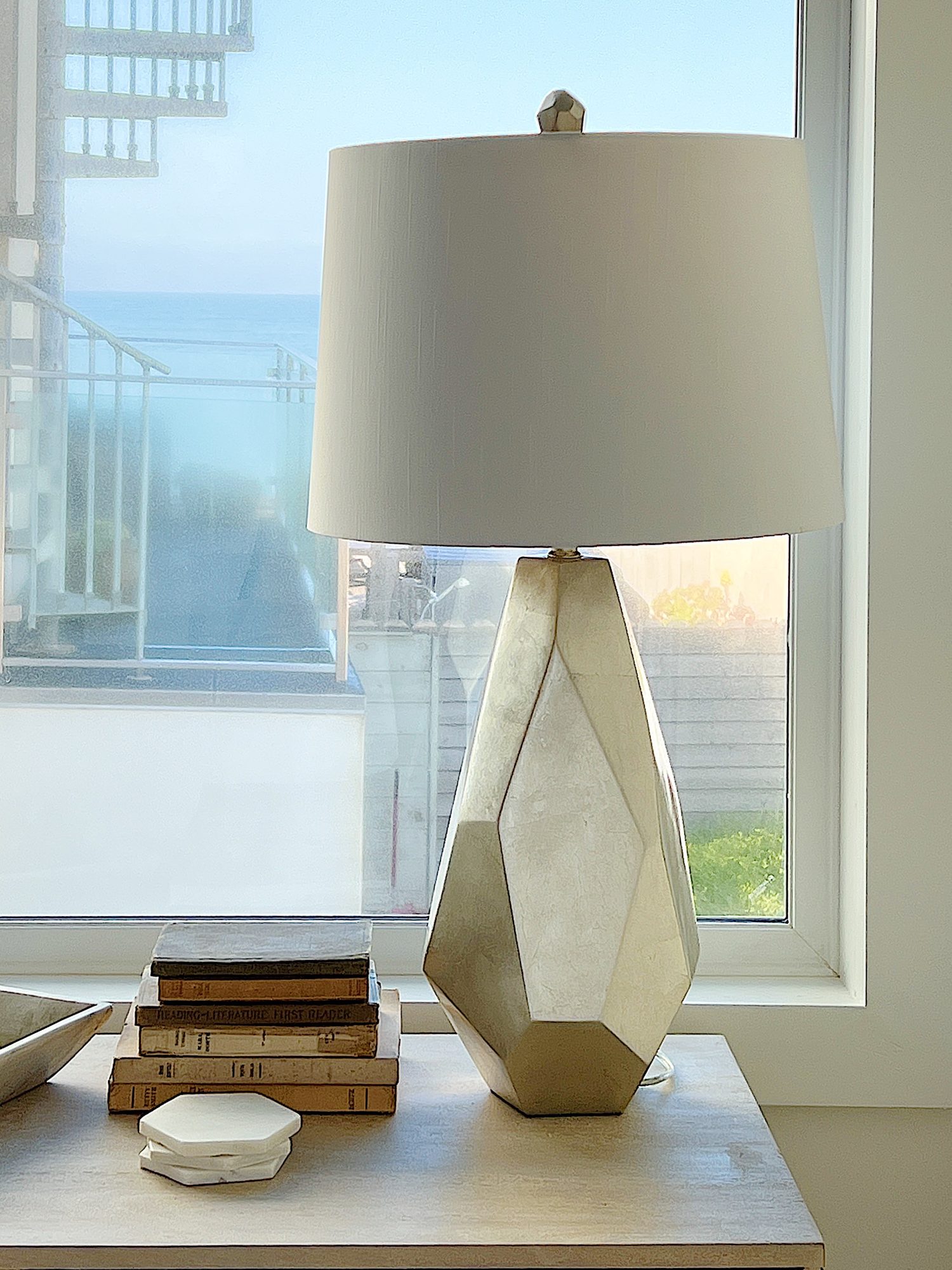A cane media cabinet with decor and a modern gold lamp and a view of the ocean.