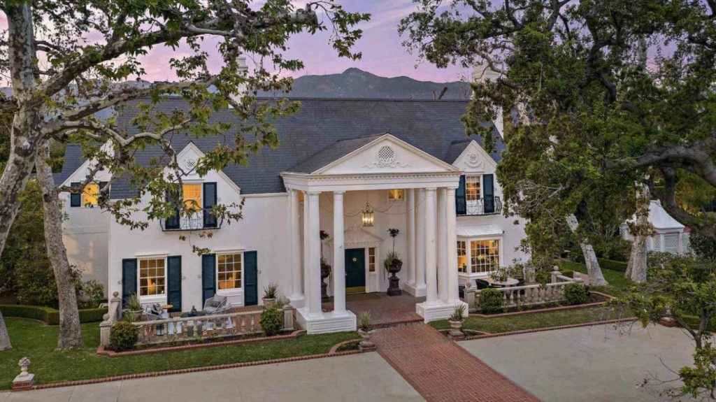 Stately federal style white columned home with black shutters and a brick path to front entrance 
