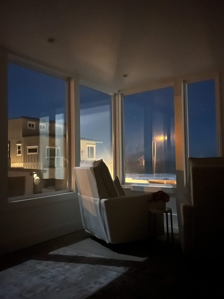 The primary bedroom in our beach house with five windows and a nightime ocean view.