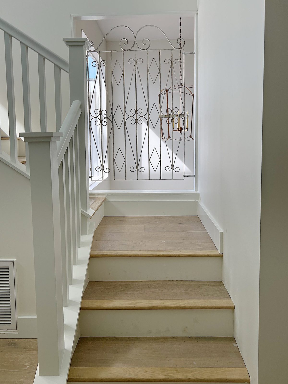A staircase with a landing and a see thru gate with a chandelier hanging behind it.