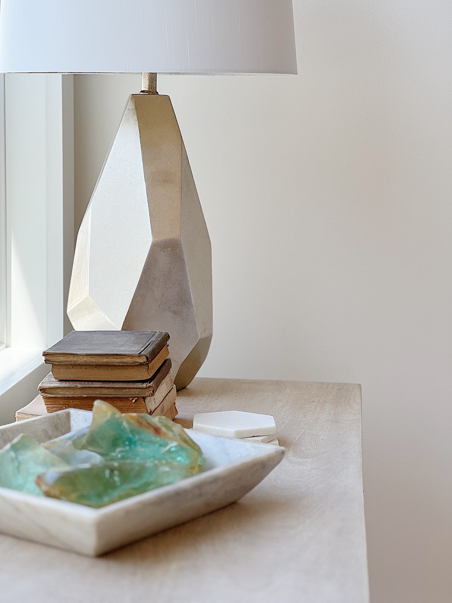 Old vintage decor books and a vintage marble container filled with old glass from a windshield factory next to a new gold lamp.