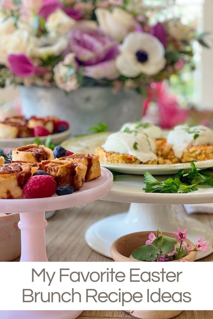 Easter brunch menu items with gluten-free cinnamon rolls, eggs benedict on crab cakes, and fresh berries sitting on cake plates on a table with flowers.