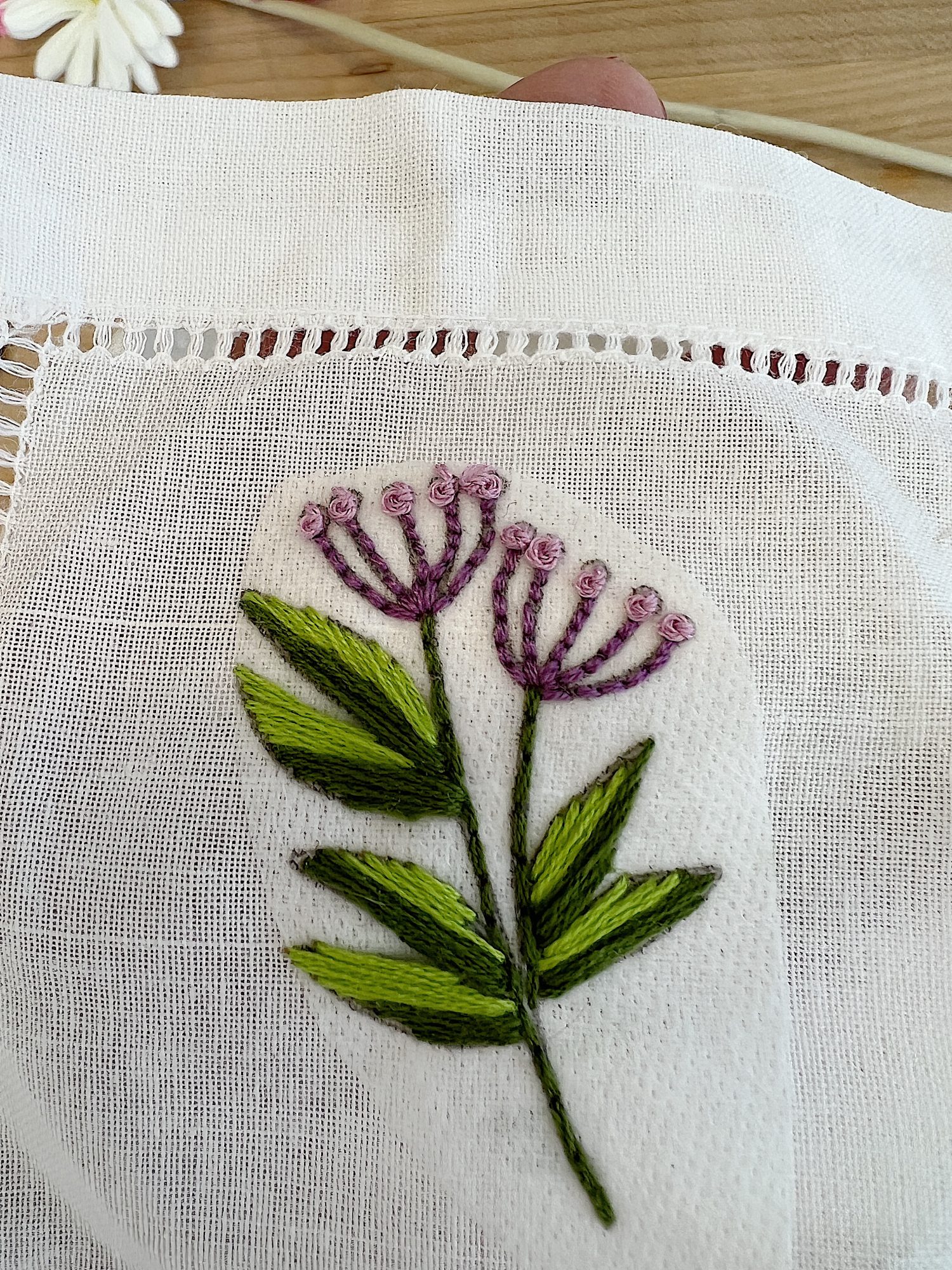 A cotton and linen hemstitched cocktail napkin, a stick-and-stitch floral embroidery pattern, an embroidery hoop, and embroidery thread.