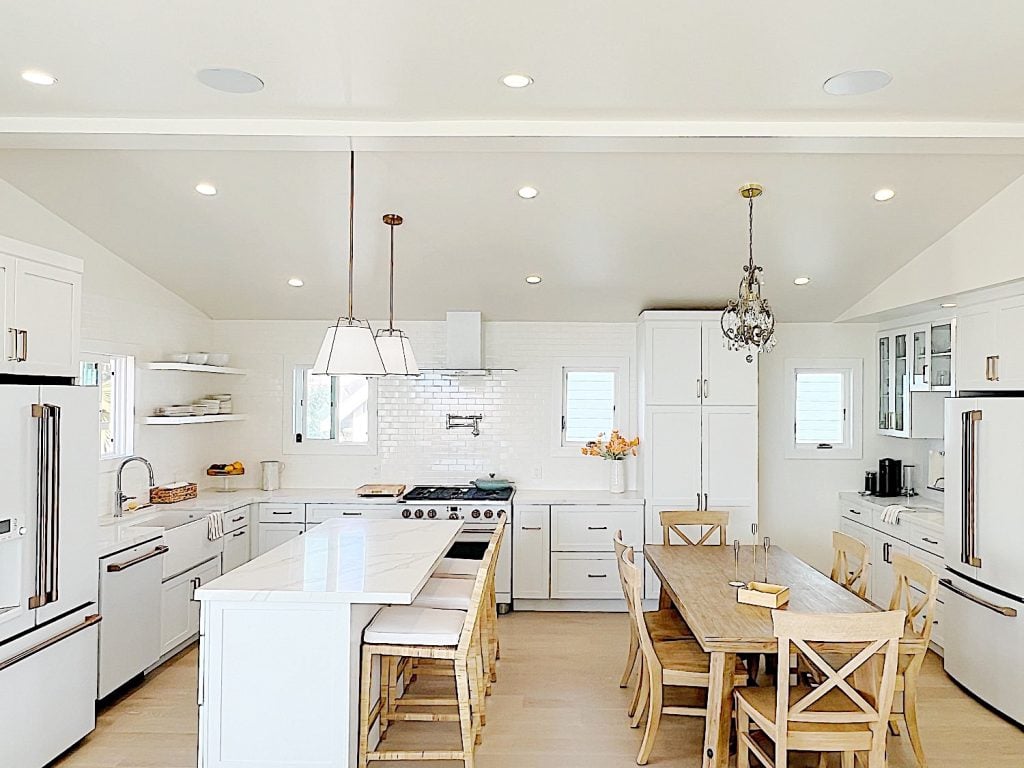 The finished beach house kitchen with white cabinets, countertops, appliances, a wood table, and an island.