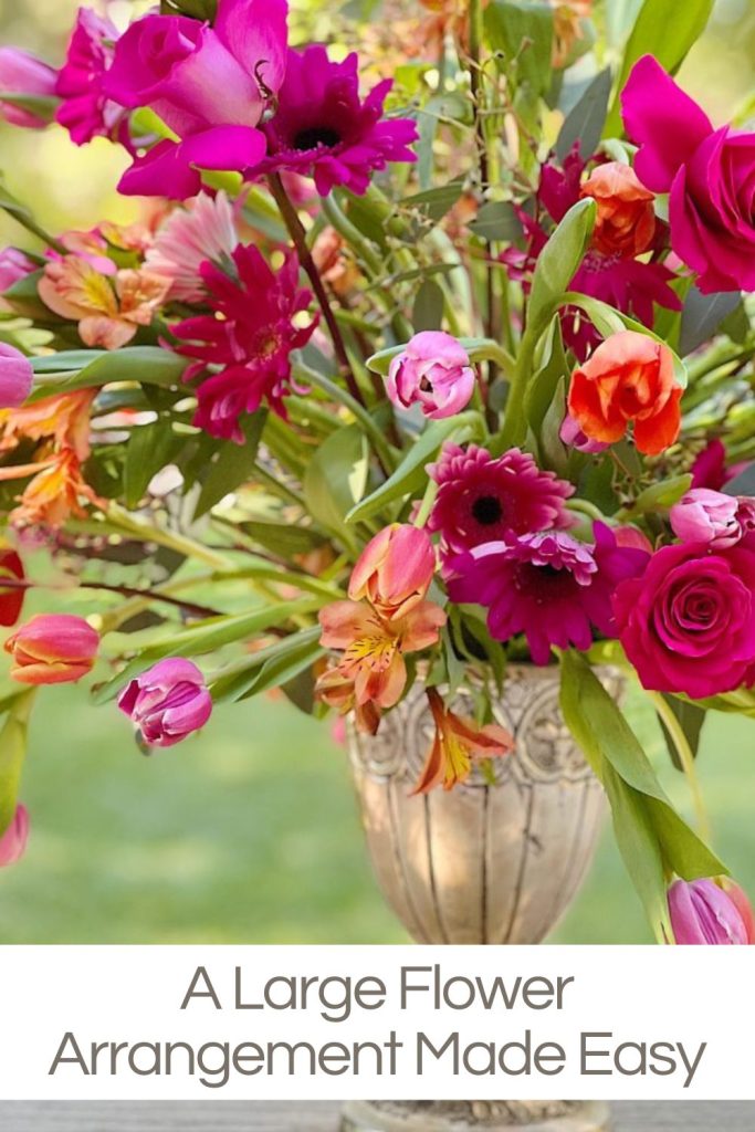 A large flower arrangement in a silver footed vase with pink and orange roses, tulips, and gerbera daisies.