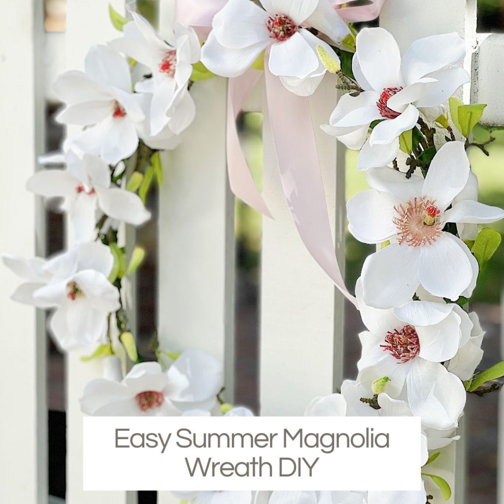 A handmade white magnolia wreath hanging on a picket fence.
