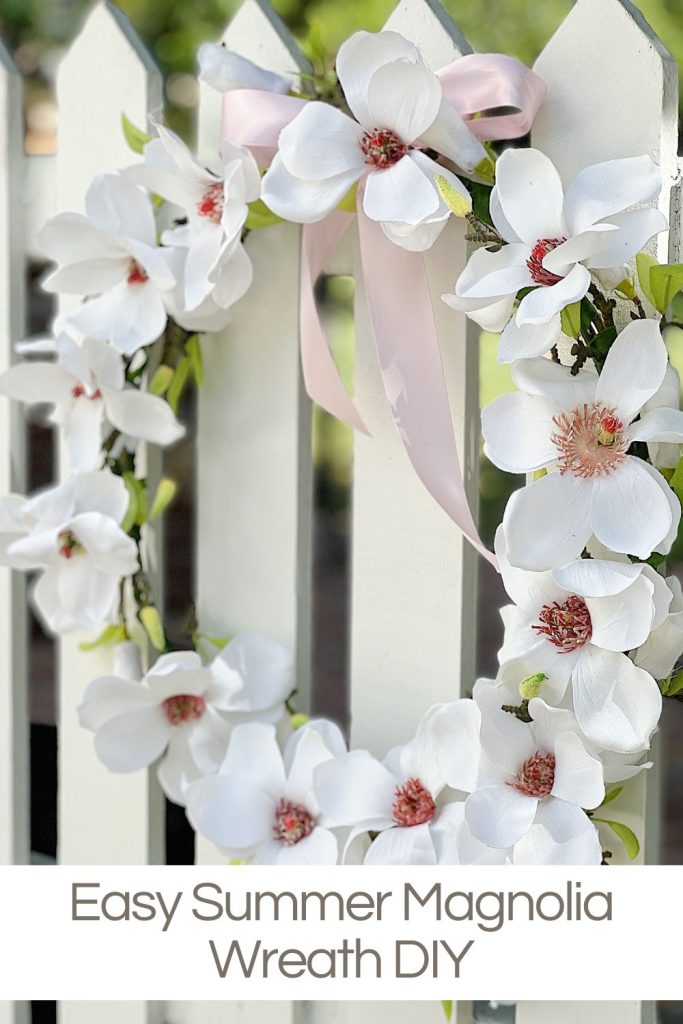 A handmade white magnolia wreath hanging on a picket fence.