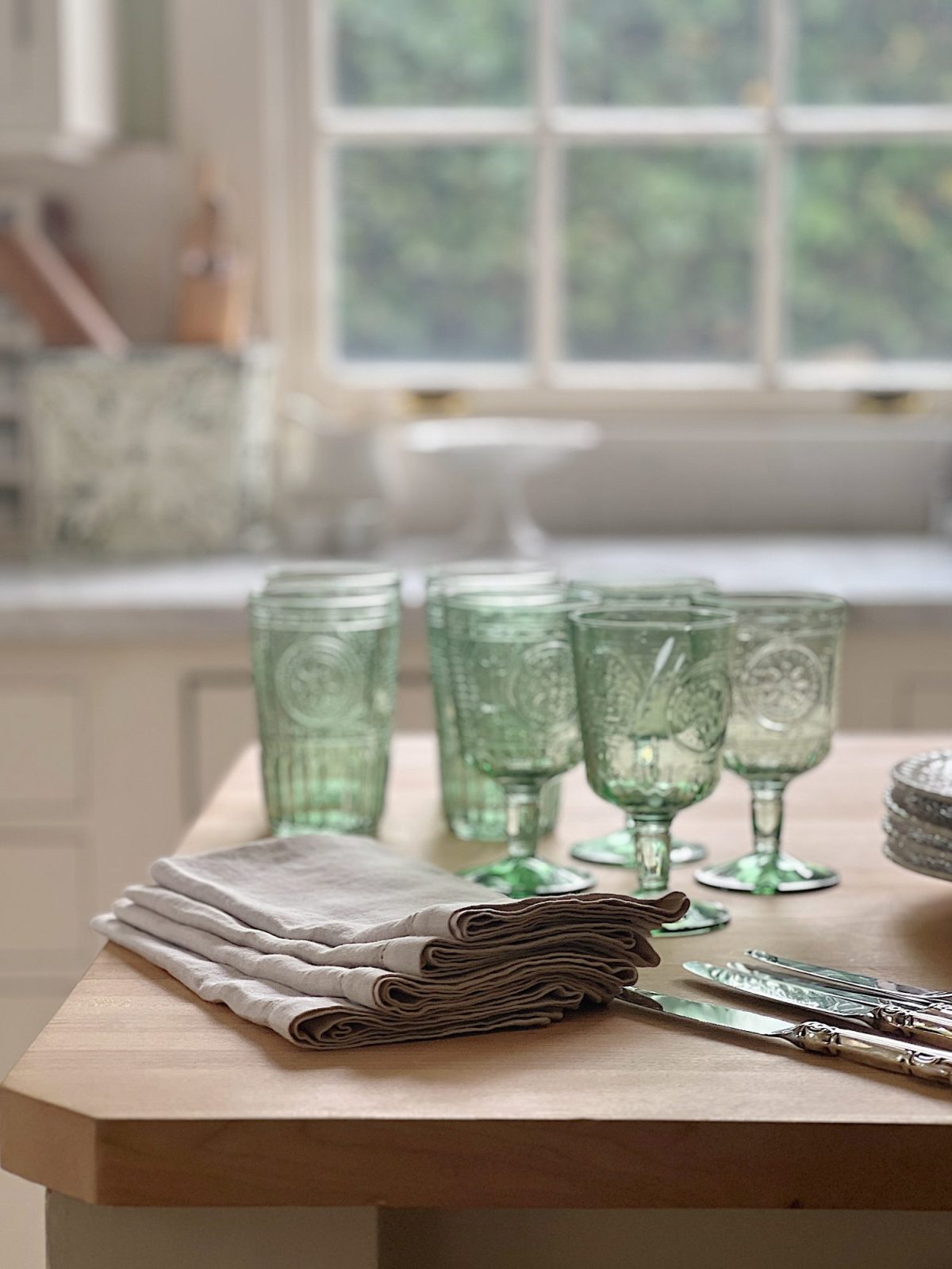 A white farmhouse kitchen with white shaker cabinets. honed marble countertops, an island with a butcher block top, and lots of farmhouse kitchen decor items.