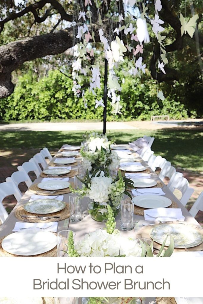 A backyard table with hanging paper butterflies, white plates, fresh flower arrangements for a bridal shower luncheon.