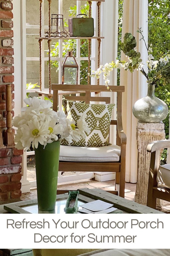An outdoor porch decorate in green and white with teak furniture, green and white pillow, and faux florals.