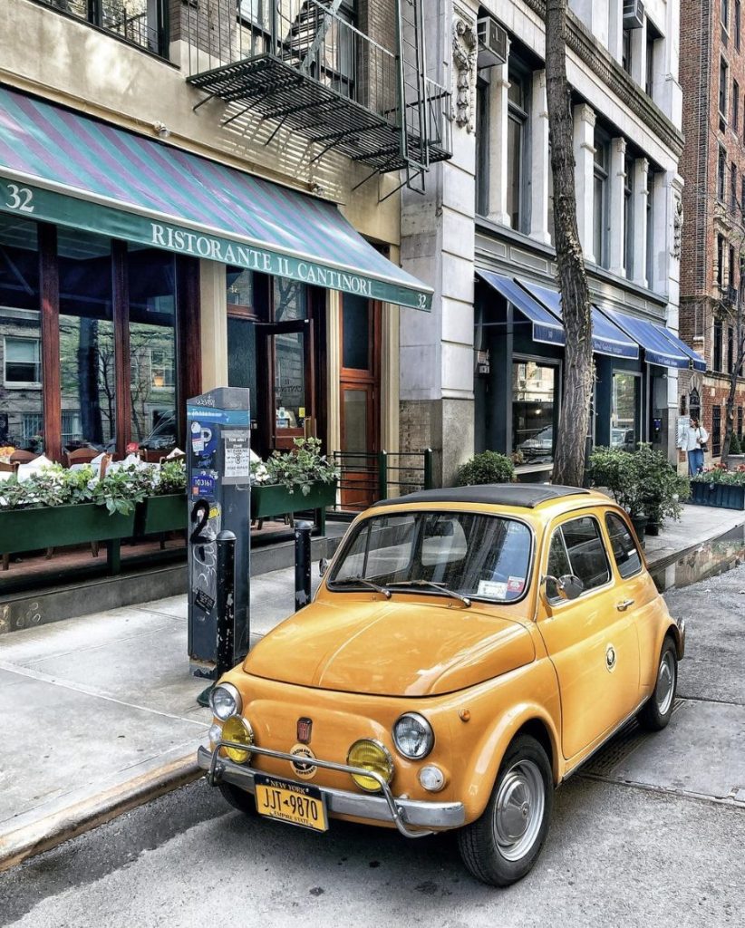 a bright yellow vintage fiat sits parked next to Ristorante El Cantinori in NYC