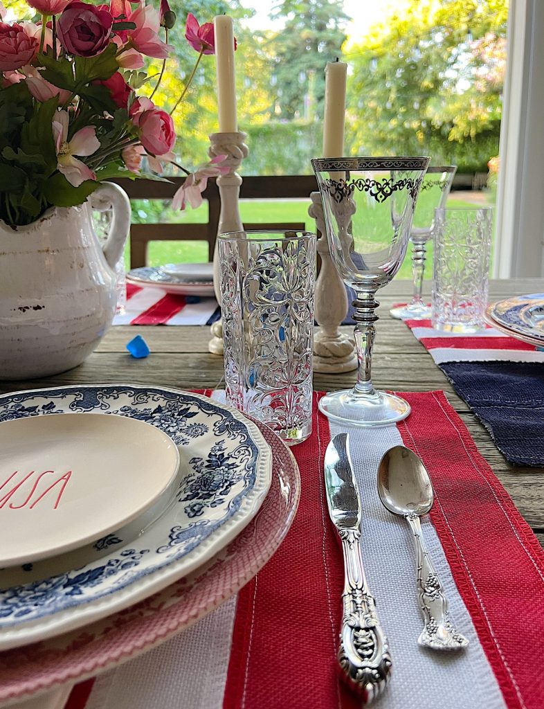 A 4th of July themed table with DIY flag placemats, red and blue and white plates, USA salad plates and candlesticks.