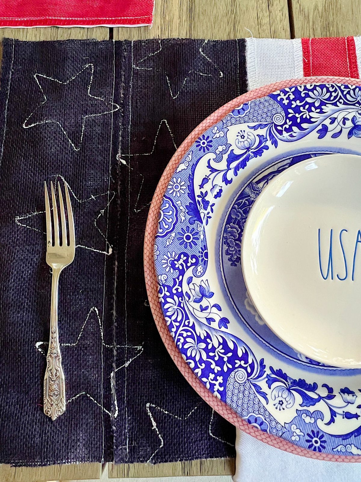 A 4th of July themed table with DIY flag placemats, red and blue and white plates, USA salad plates and candlesticks.