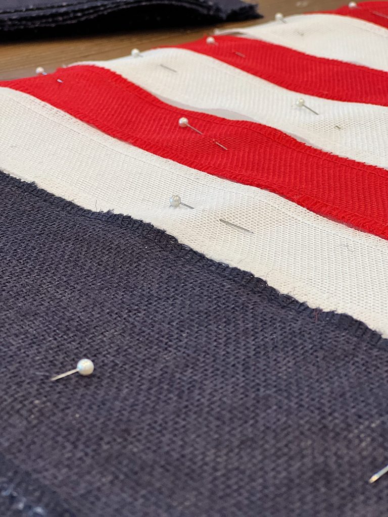 Pinning the navy, red, and white burlap ribbon on to the white cotton fabric.