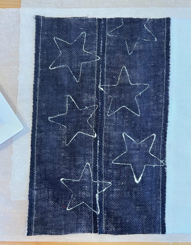 Using a cookie cutter and white paint to cretae white stars o the blur burlap.