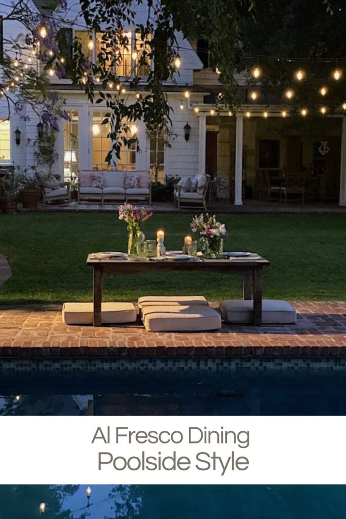 A low table set in the back yard next to the pool with hanging lights and cushions on the patio for comfort.