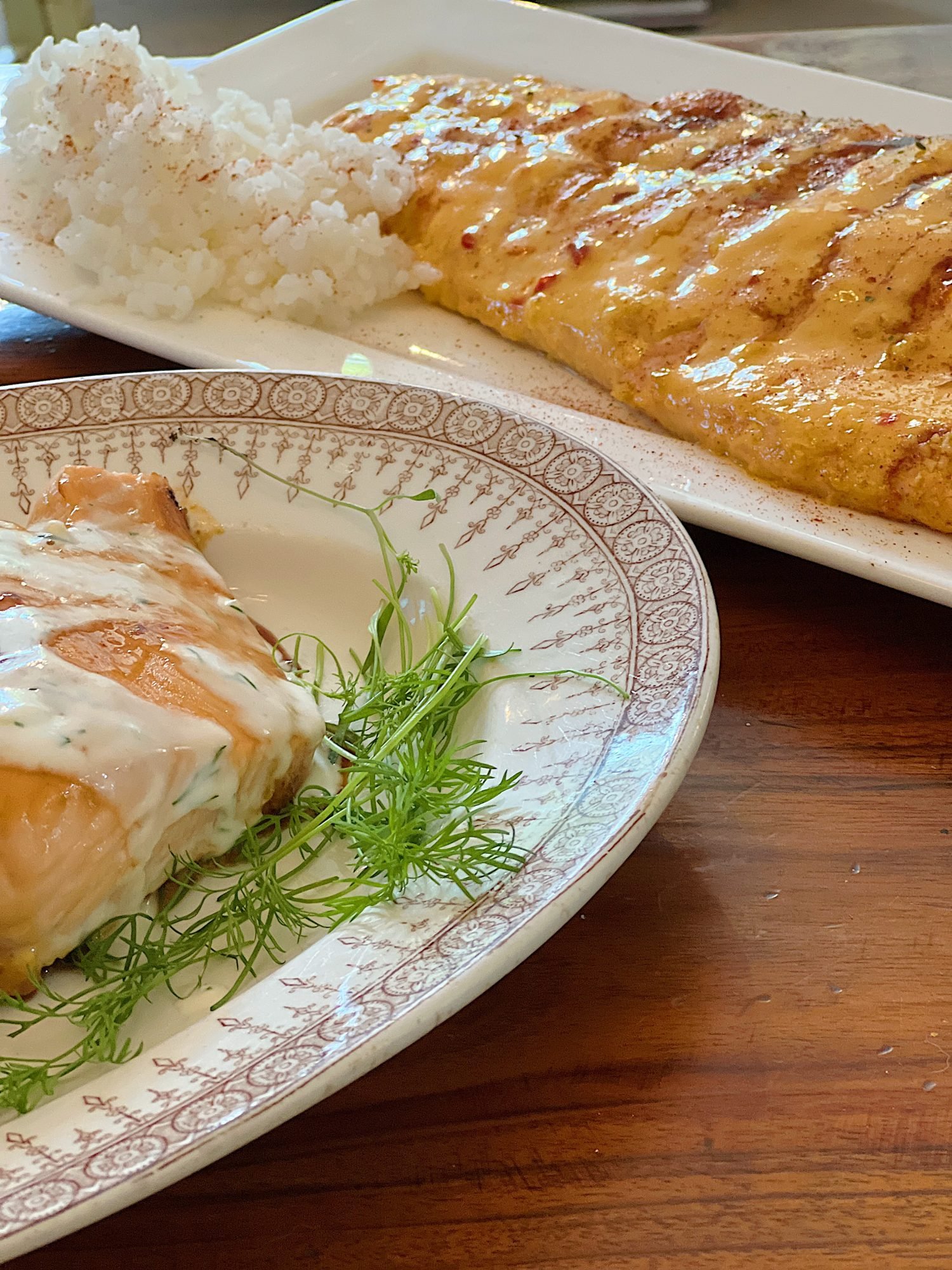 Two plates of salmon including pellet grilled honey salmon with lemon dill sauce and bang bang salmon.