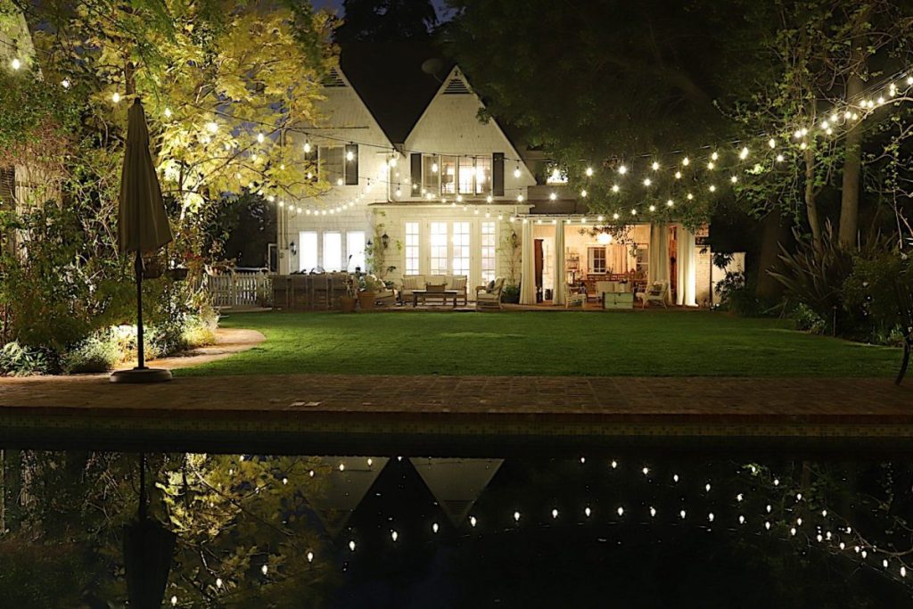 The backyard of our 100 year old home with hanging string lights and a reflection in the pool.
