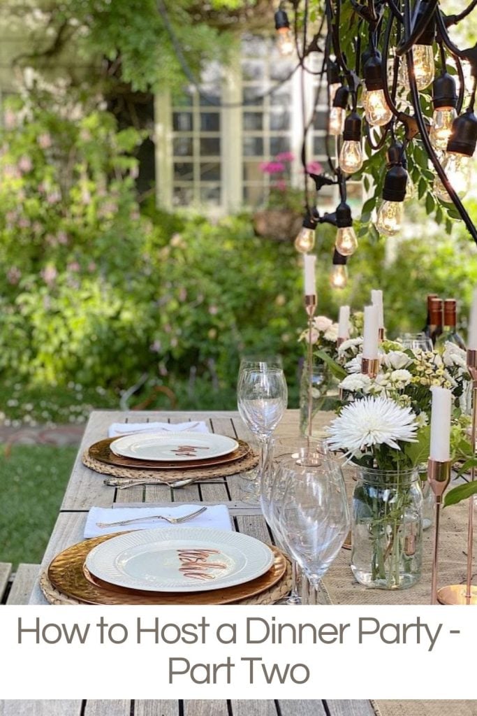 An outdoor table set with copper chargers, a white place, place cards, candles and beautiful flowers and hanging lights.