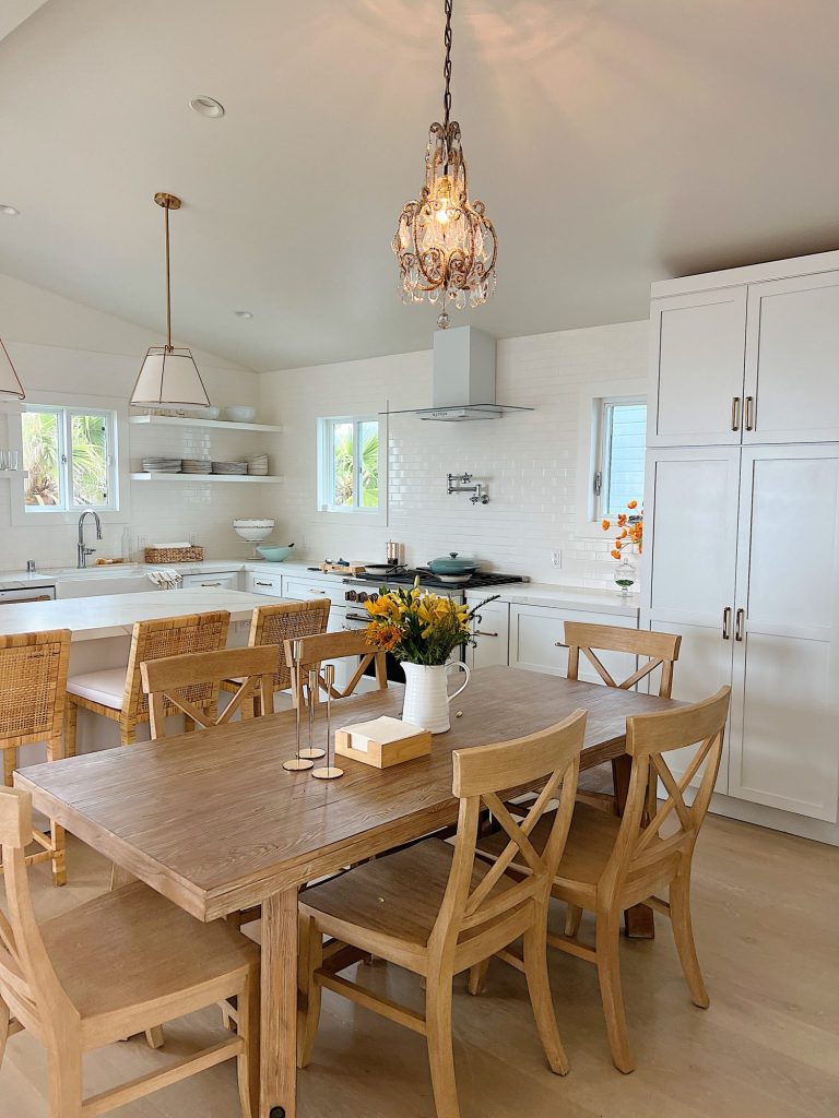 Our kitchen at the beach house with a hanging vintage chandelier, table and chairs, white cabinets, tile, and countertops.