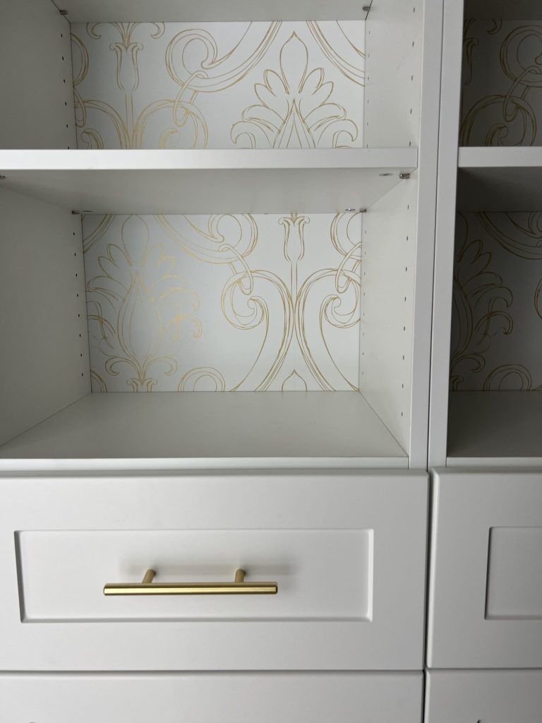 New built in white closets with gold handles and white and gold wallpaper on the walls.