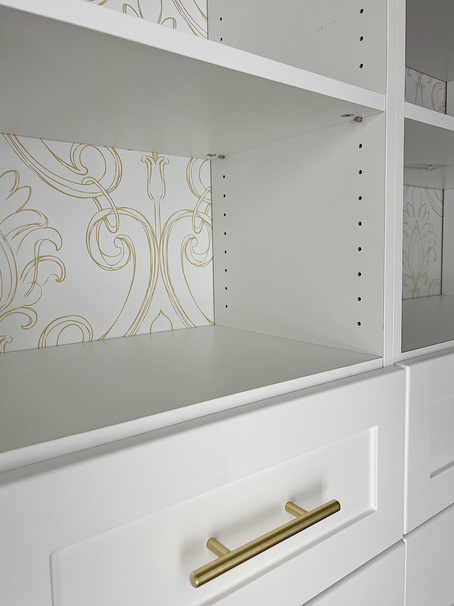 New built in white closets with gold handles and white and gold wallpaper on the walls.