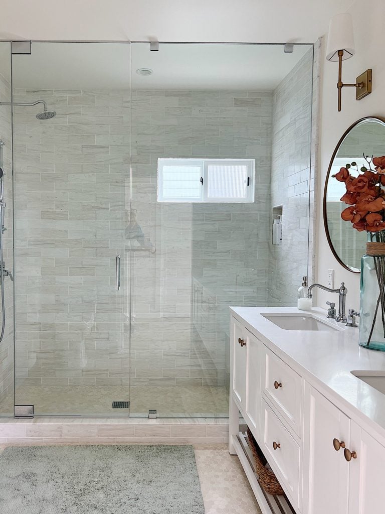 A newly constructed primary bathroom with a double sink vanity, marble tile shower, and decor.