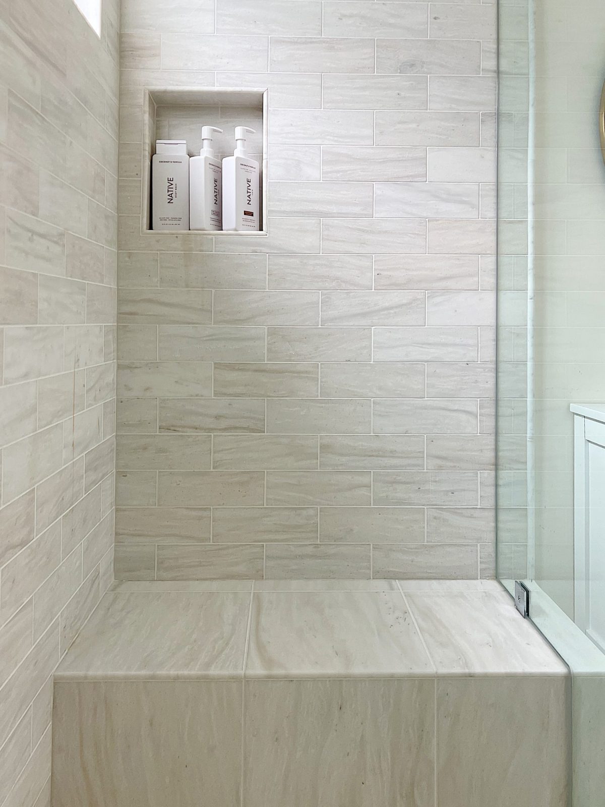 A newly constructed primary bathroom with a double sink vanity, marble tile shower, and decor. The marble tile shower has a seat.