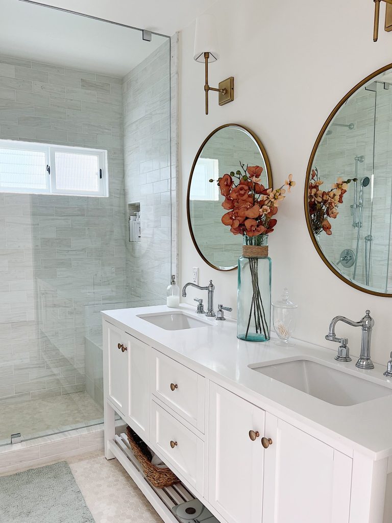 A newly constructed primary bathroom with a double sink vanity, marble tile shower, and decor.