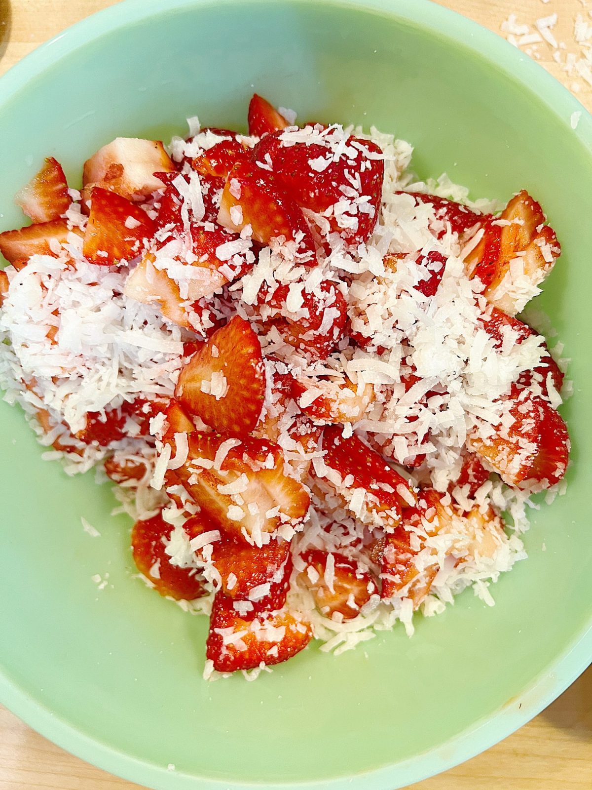 A green bowl filled with cut fresh strawberries and flaked coconut.