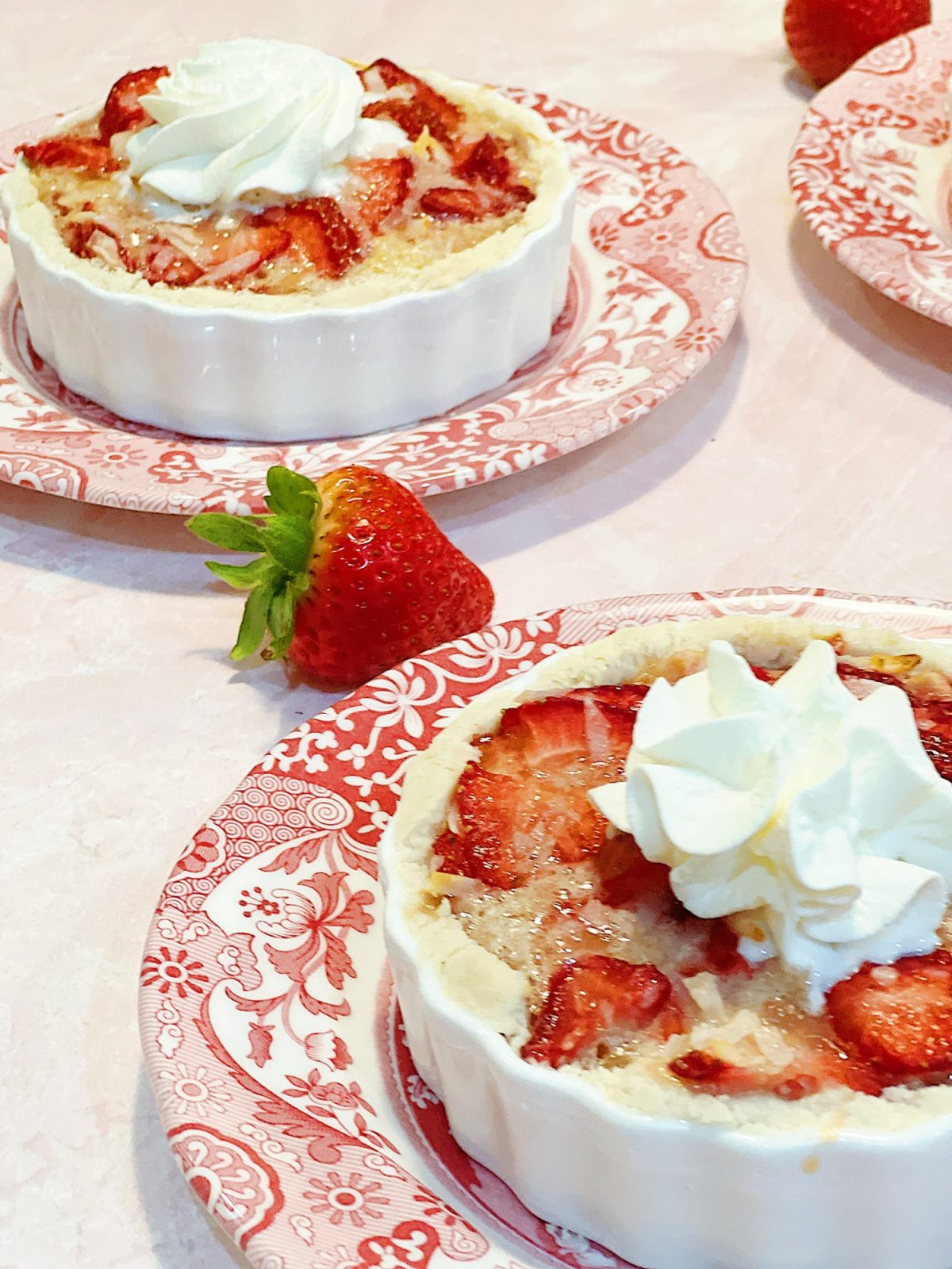 A homemade strawberry coconut tart with a delicious crust and whip cream dollop served in a white tart pan on a red and white plate.