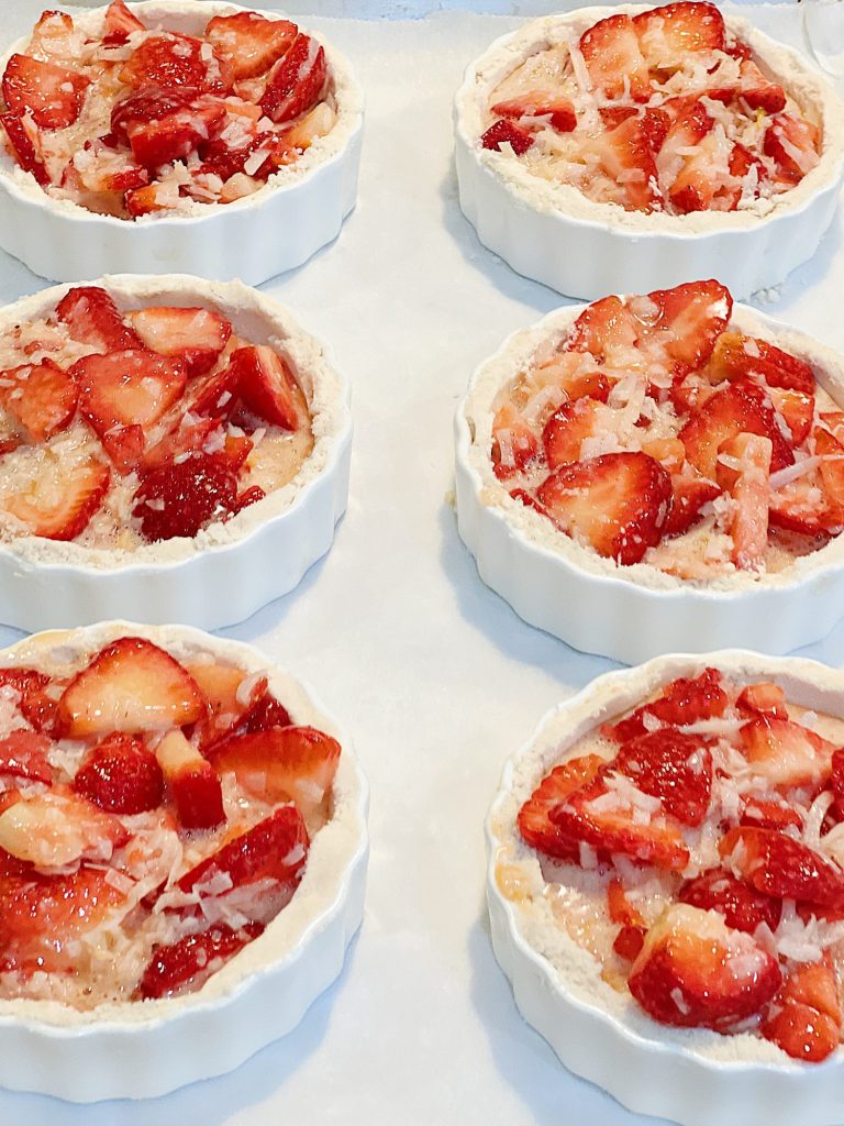 A homemade strawberry coconut tart with a delicious crust served in a white tart pan on a red and white plate.