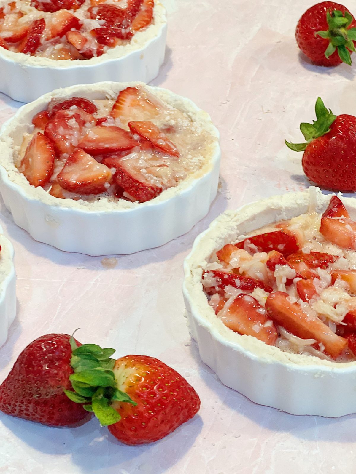 A homemade strawberry coconut tart with a delicious crust served in a white tart pan on a red and white plate.