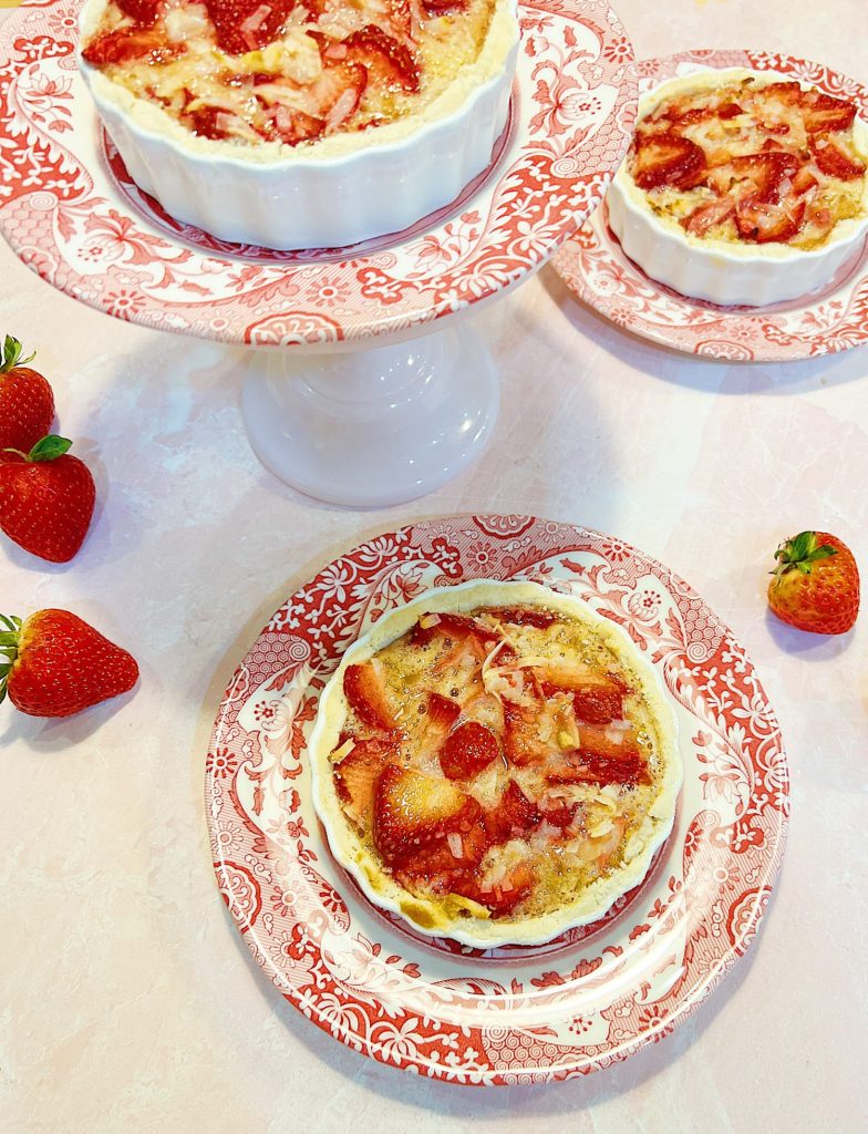 A homemade strawberry coconut tart with a delicious crust served in a white tart pan on a red and white plate.