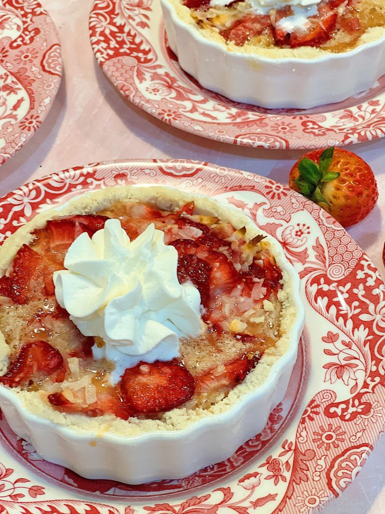 A homemade strawberry coconut tart with a delicious crust and whip cream dollop served in a white tart pan on a red and white plate.