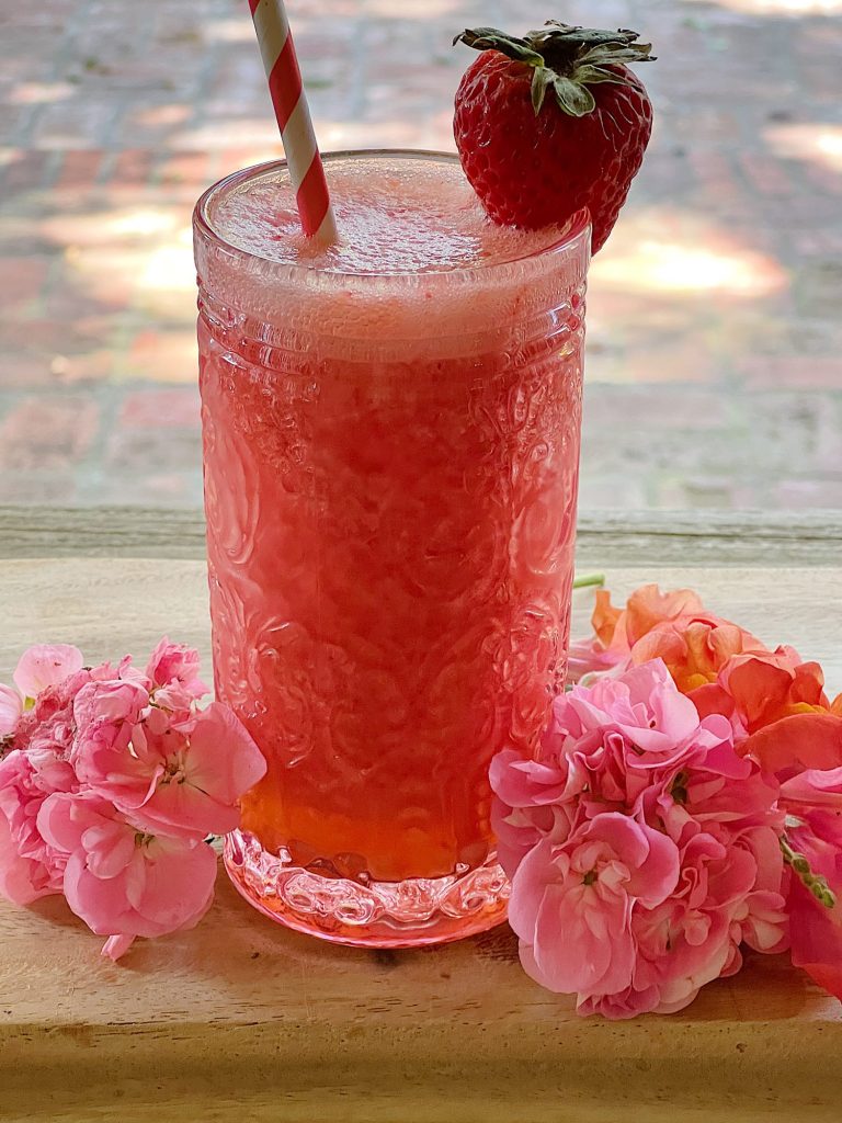 A freshly made Strawberry Daquiri Refreshing Summer Mocktail in a glass with a paper straw and strawberry garnish.