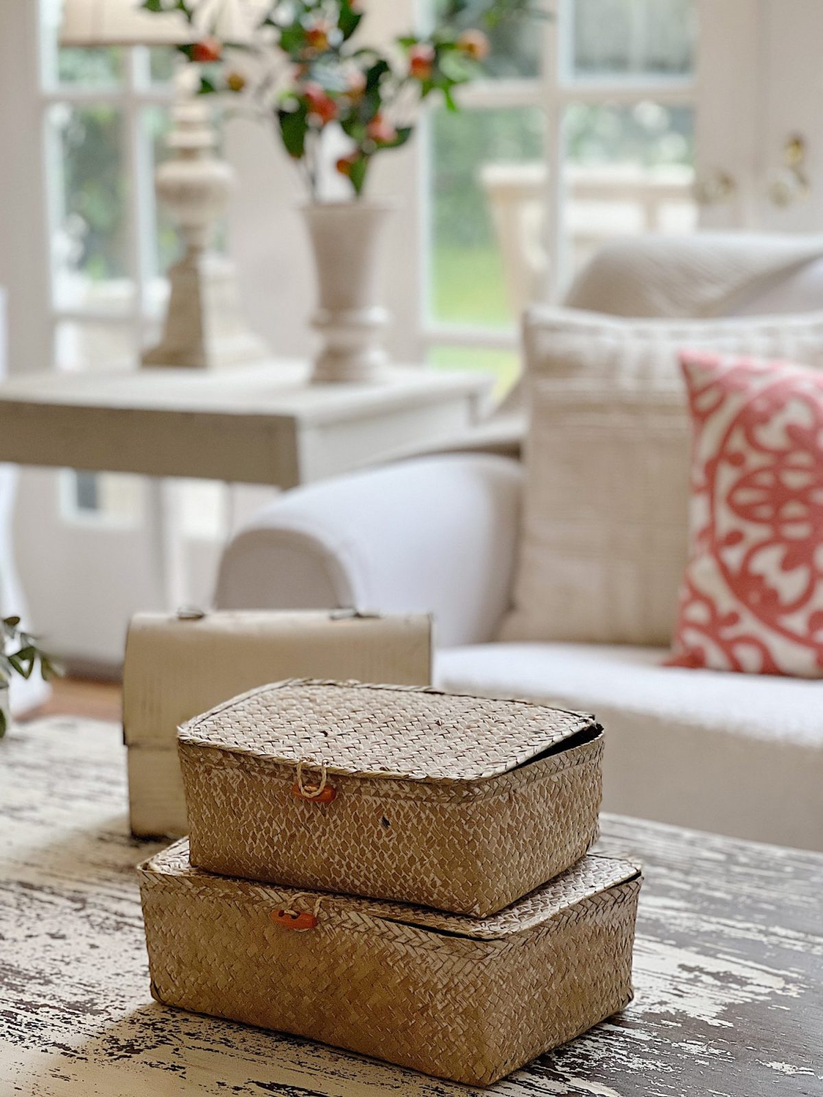 A white couch and assorted pillows and a vintage hanging chandelier are also in the family room. There are peach blossoms in a vase and various neutral decor items on the coffee table.