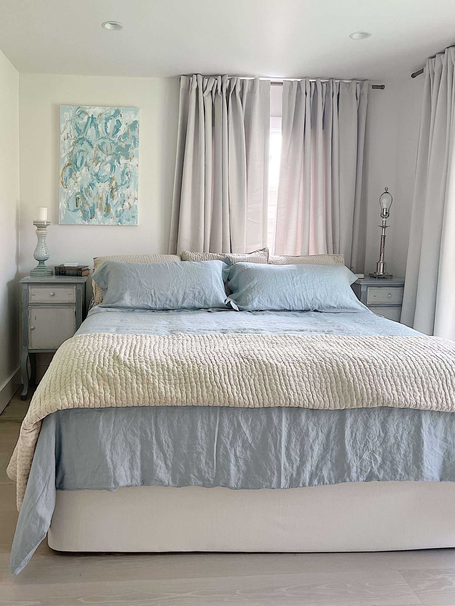 Another bedroom with a king bed, linen comforter and abstract art on the wall.