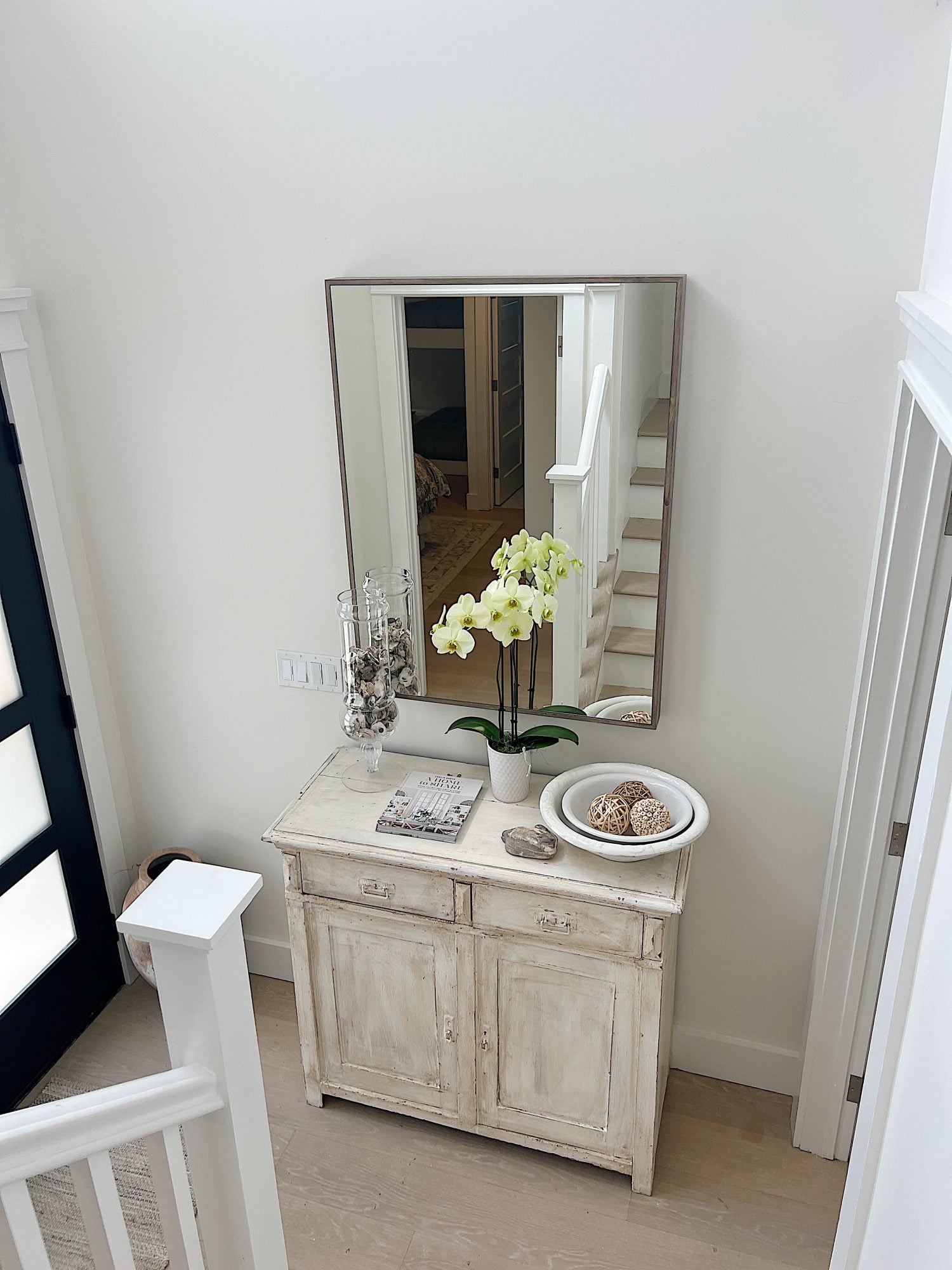 The entry way in the beach house with a vintage cabinet, new mirror and various vintage decor items.
