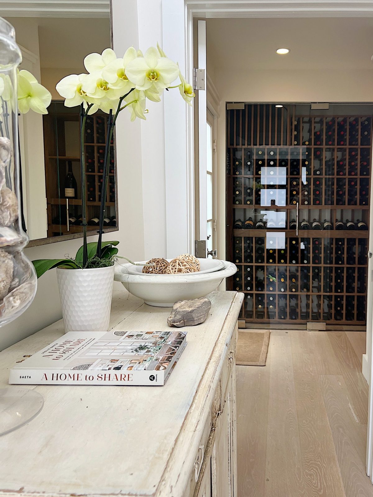The entryway of our beach house with a vintage cabinet, plant, and decor accessories with a wine cellar in the background.