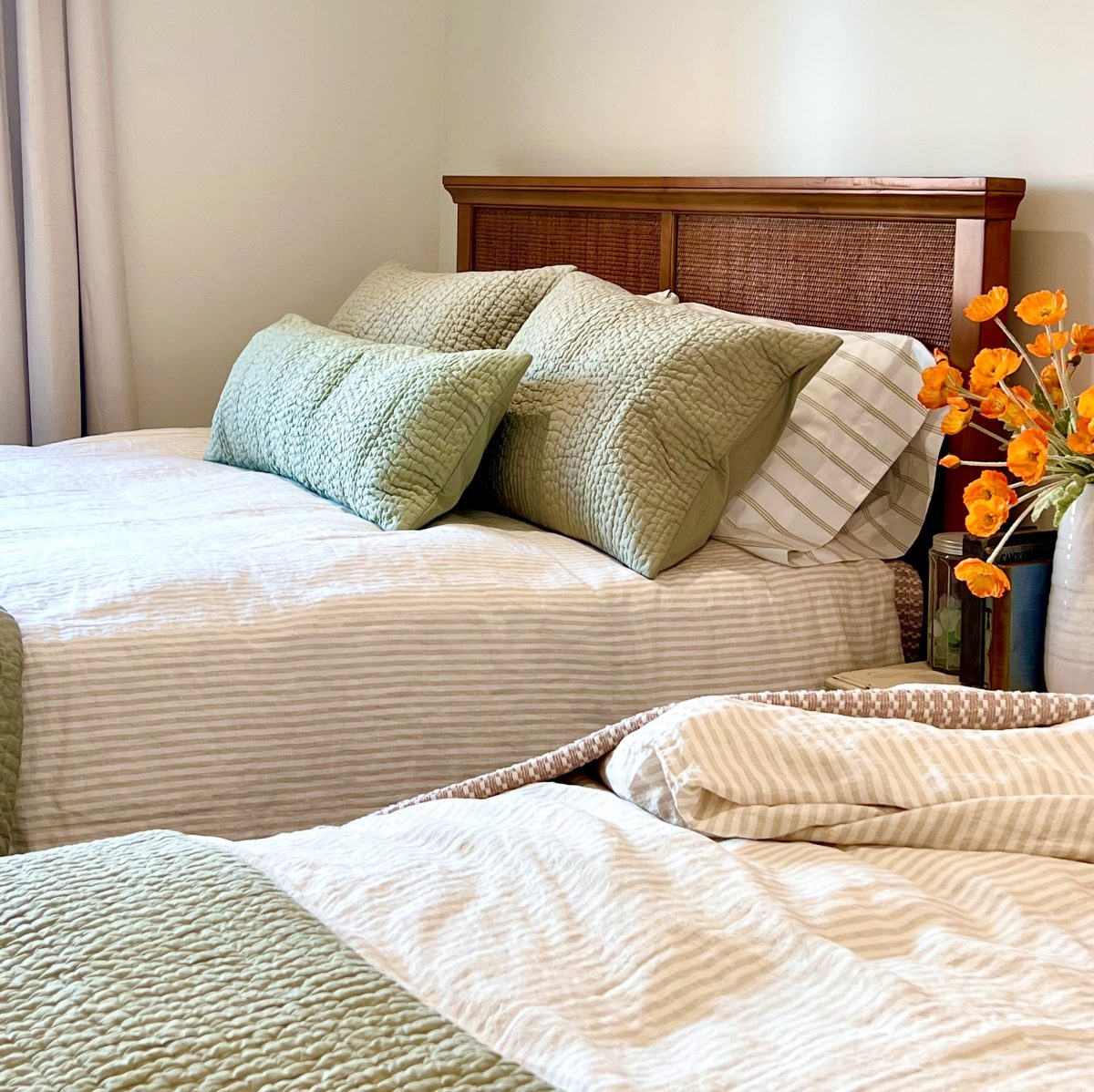 A bedroom at the beach house with two queen beds with sage green and cream bedding.