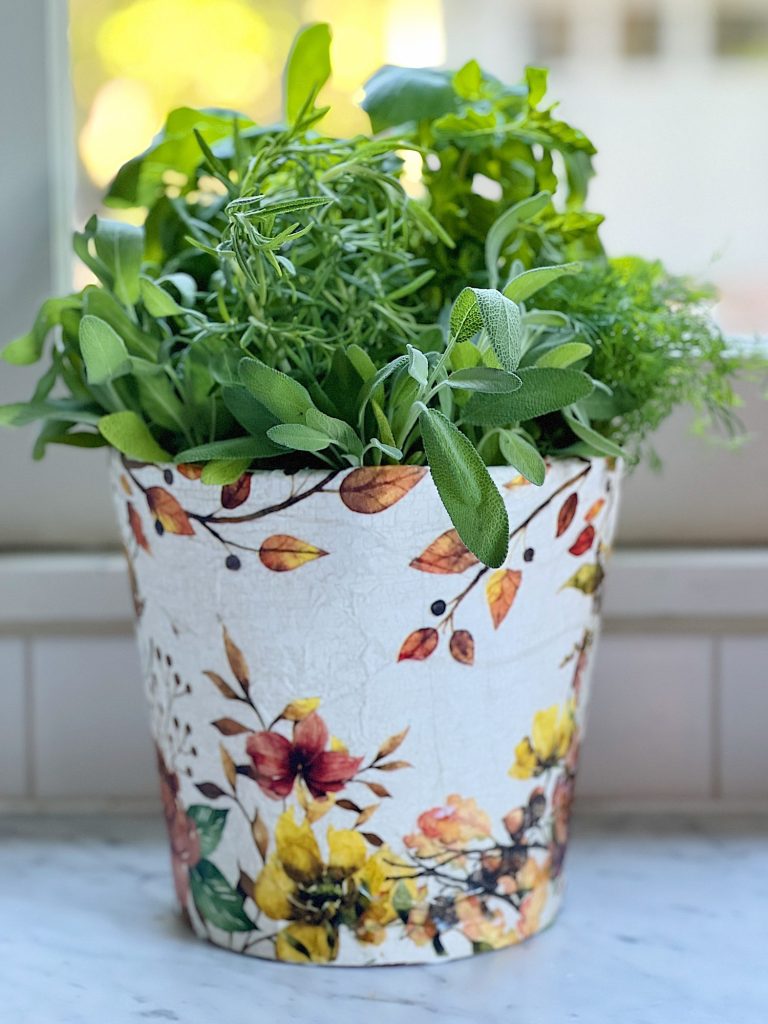A terra cotta pot painted and covered with a beautiful paper napkin filled with fresh herbs for cooking.