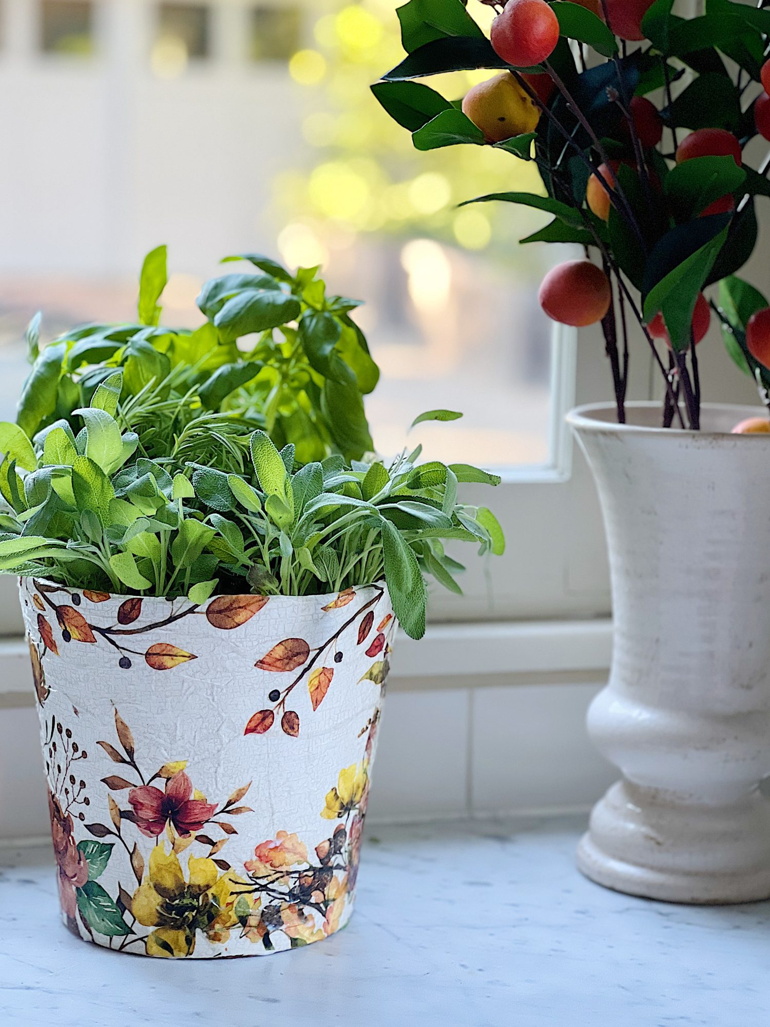 A terra cotta pot painted and covered with a beautiful paper napkin filled with fresh herbs for cooking.