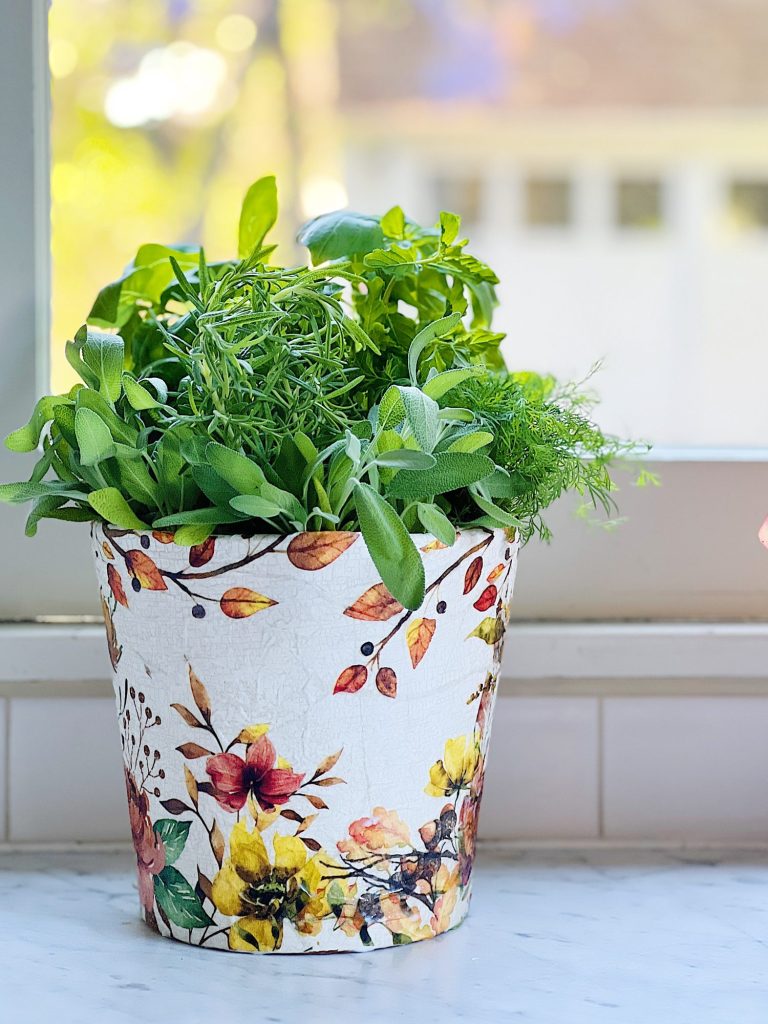 A terra cotta pot painted and covered with a beautiful paper napkin filled with fresh herbs for cooking.