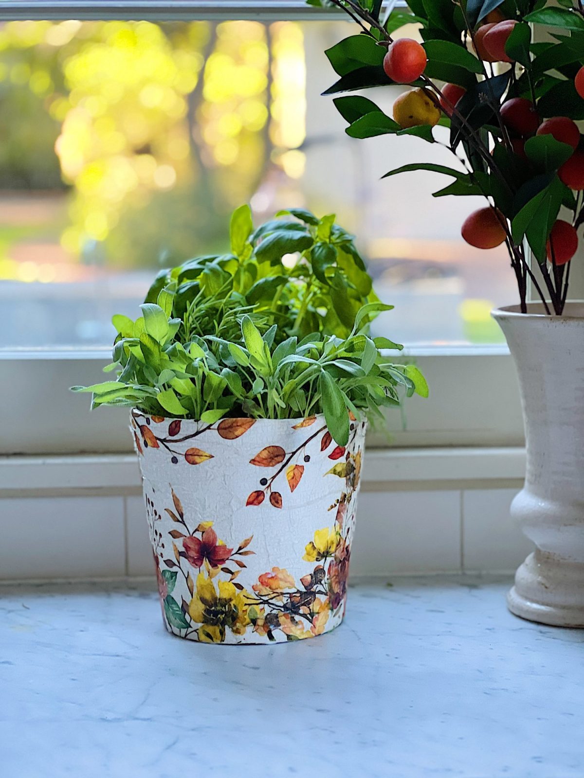 A terra cotta pot painted and covered with a beautiful paper napkin filled with fresh herbs for cooking.