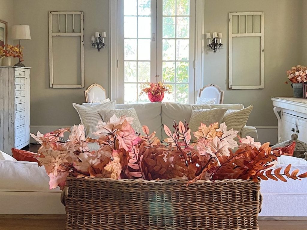 A living room decorated with fall decor including faux leaves, fall pillows, and fall flower arrangements.